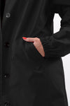 A person in a LUXE BLACK WATERPROOF WINDBREAKER by looselyboho, featuring black buttons and elastic cuffs, showcases a hand with red nails tucked into the side pocket. The water-resistant design suits any weather, set against a plain white background.