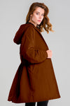 A woman with long hair models the looselyboho BURNT BROWN WINDBREAKER. It features a cinched waist, pockets, and an adjustable hood made from lightweight, water-resistant fabric. She stands sideways, glancing over her shoulder against a plain background.