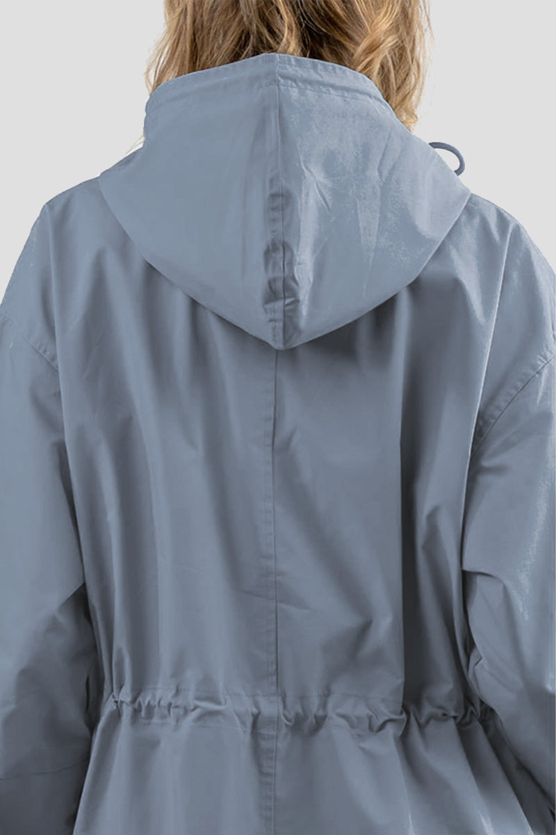 A person with light brown hair is seen from behind wearing The Windbreaker Jacket's POWDER BLUE WINDBREAKER. The water-resistant jacket features a loose fit with a cinched detail at the waist, set against a plain gray background.