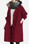 A person in a long red coat featuring black buttons and a gray scarf stands with their hands tucked in pockets. The white top beneath the looselyboho Burgundy Blossom Windbreaker highlights its floral-patterned collar lining.