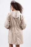 A person with curly hair is seen from the back wearing a stylish rain-jacket. The BISCUIT BEIGE WINDBREAKER by looselyboho, designed with a cinched waist and long sleeves, boasts an adjustable hood and lightweight waterproof material. The background is plain white.